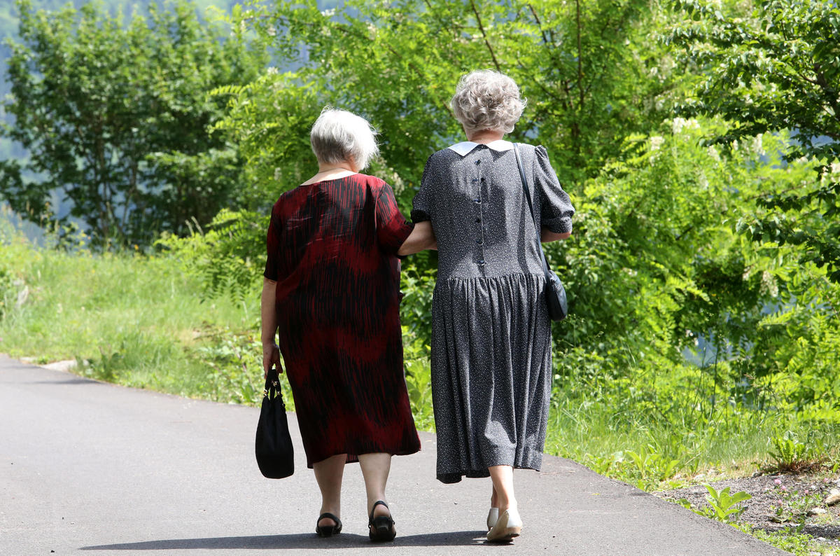 Due donne anziane si tengono per mano passeggiando lungo una strada